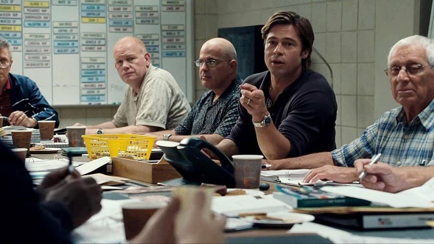 Still from Moneyball of Billy Beane (played by Brad Pitt) leading a room of scouts, used to illustrate assigning the right resource to the right job instead of defaulting to the most expensive option